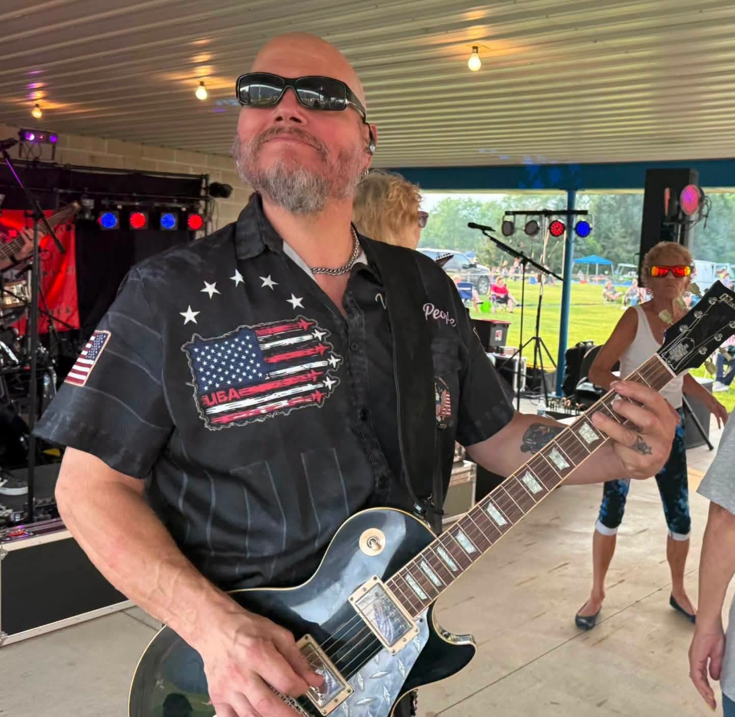 DBC guitarist performing in front of the neon Dart Board Compromise sign